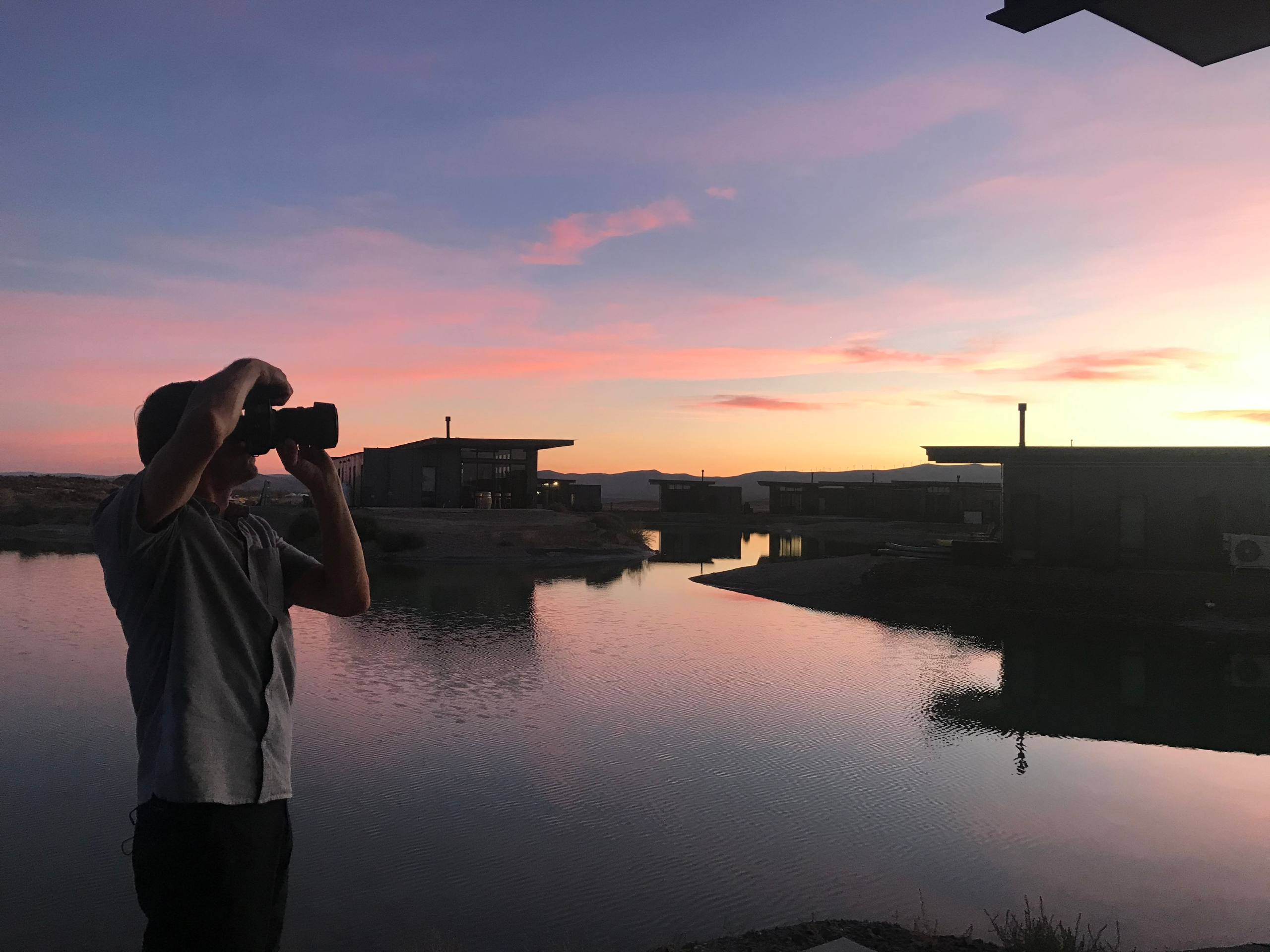 Ron, Creative Director, shooting the sunset over a body of water with houses and mountains in the background.